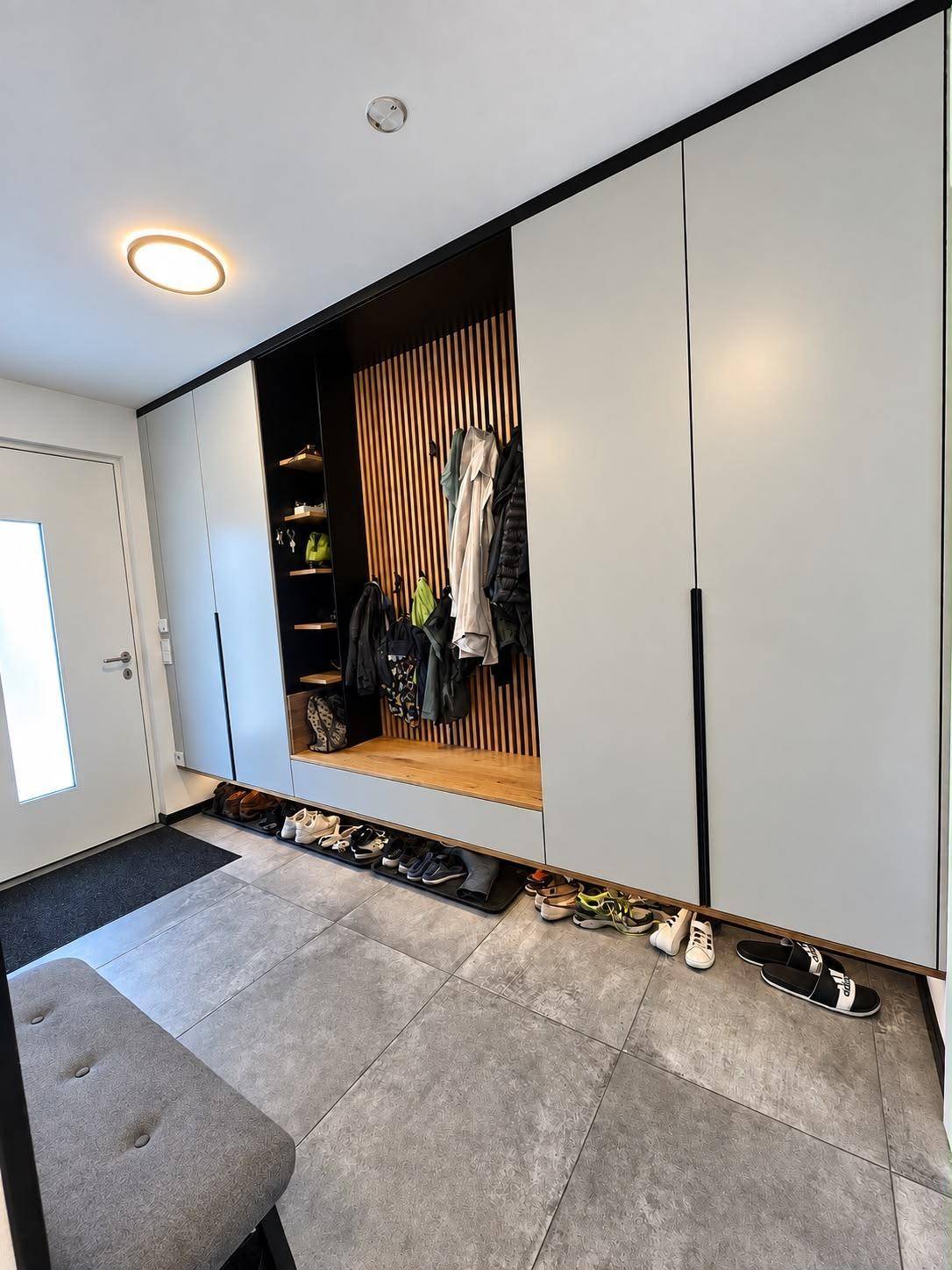 Moderner Eingangsbereich mit integrierter Garderobe, Sitzbank und großformatigen Fliesen.