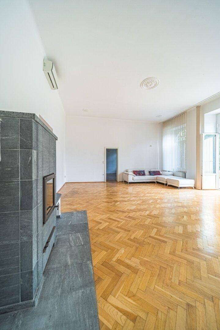 Geräumiges Wohnzimmer mit Fischgrätparkett, modernem Kaminofen und bequemer Sofalandschaft.