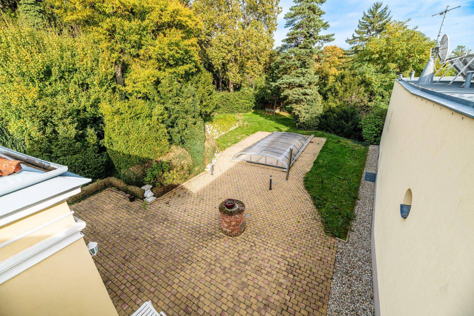 Vogelperspektive auf die gepflasterte Terrasse mit überdachtem Pool und umgebendem Gartenbereich.