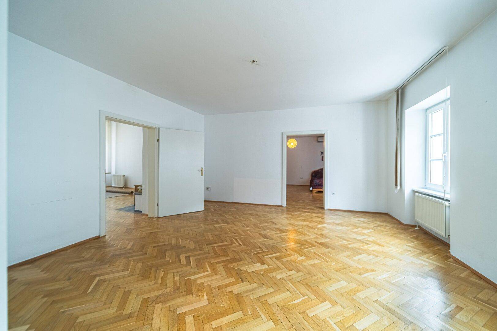 Geräumiges Wohnzimmer mit klassischem Fischgrätparkett und mehreren Türen zu angrenzenden Räumen.