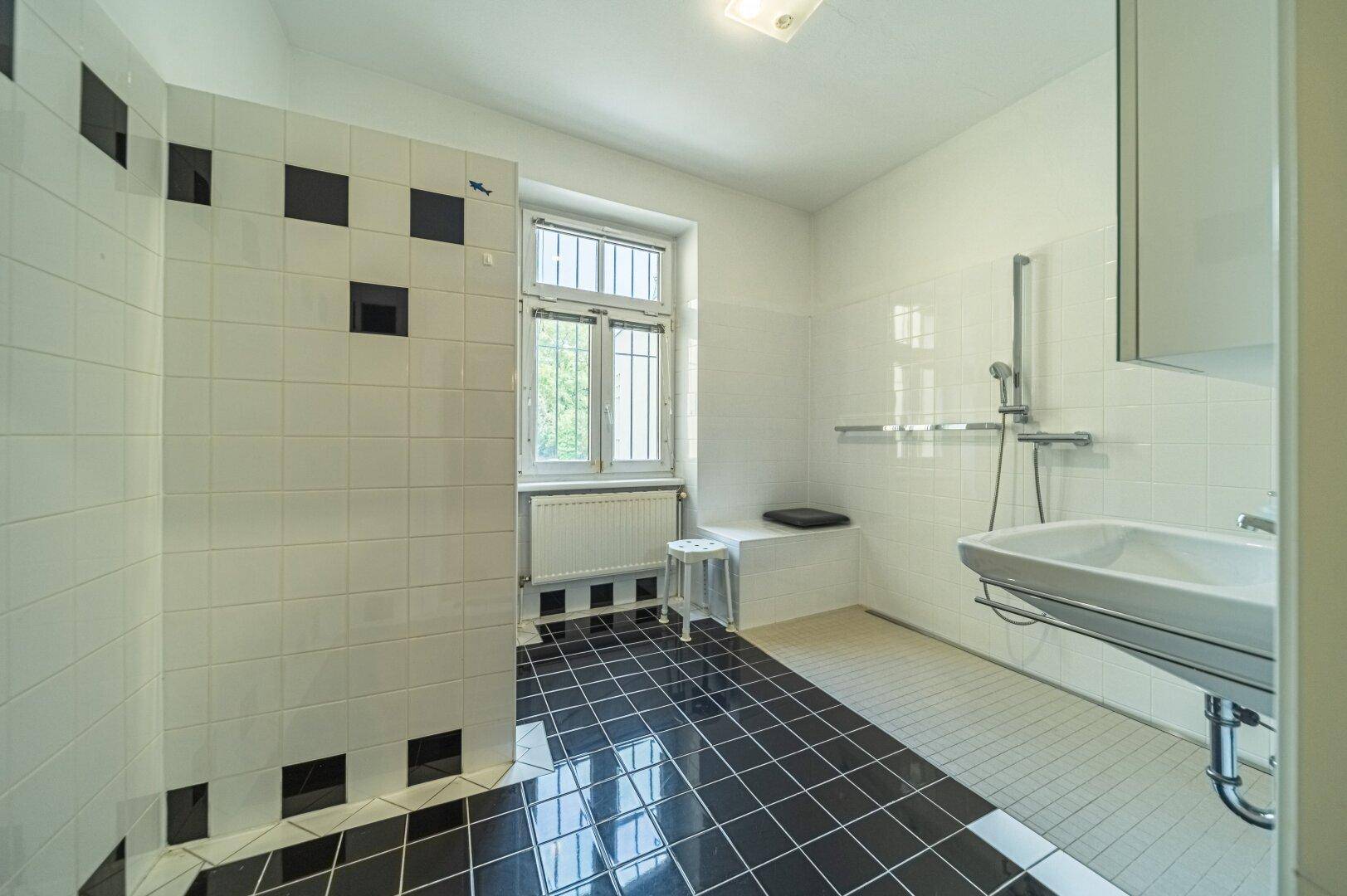 Badezimmer mit schwarz-weißen Fliesen, ebenerdiger Dusche und Fenster für Tageslicht.