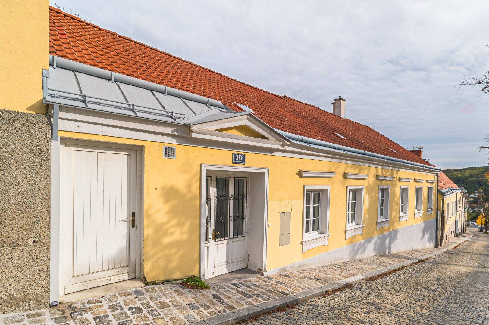 Historisches Gebäude mit gelber Fassade und rotem Ziegeldach an einer gepflasterten Straße.