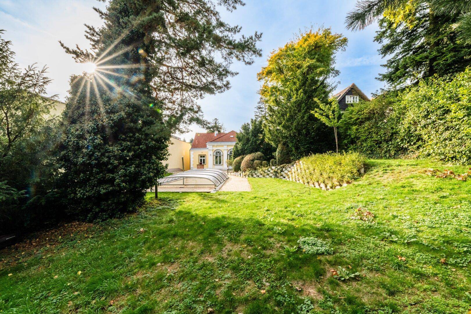 Weitläufiger Garten mit altem Baumbestand und Blick auf das historische Gebäude im Hintergrund.
