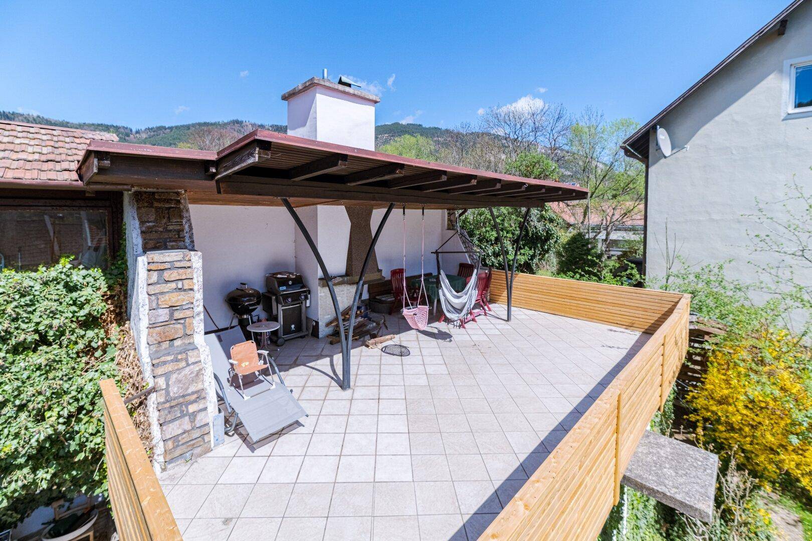 Große geflieste Terrasse mit Überdachung, Grillbereich und Hängematte für Entspannung.