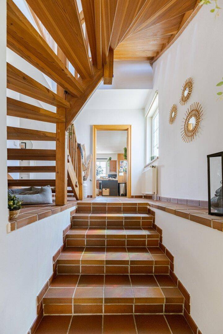 Eingangsbereich mit Terrakotta-Fliesenboden und Holztreppe, die in die obere Etage führt.