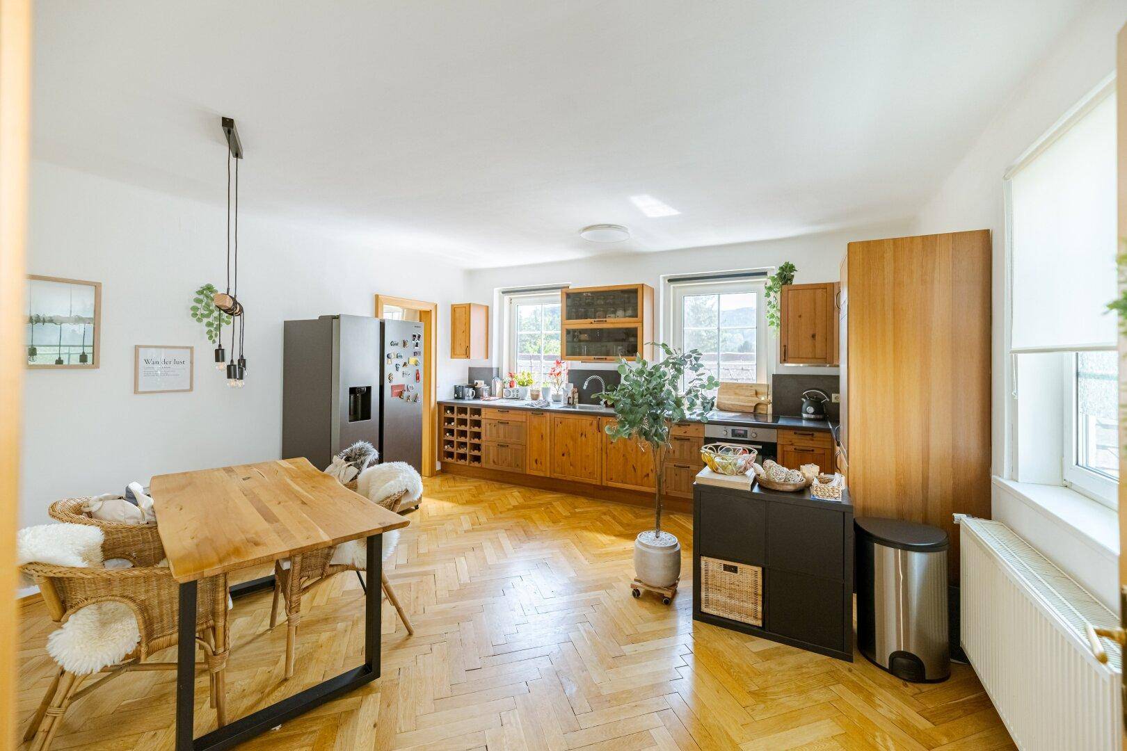 Helle Wohnküche mit Holzboden, Esstisch und Blick ins Grüne durch die Fenster.