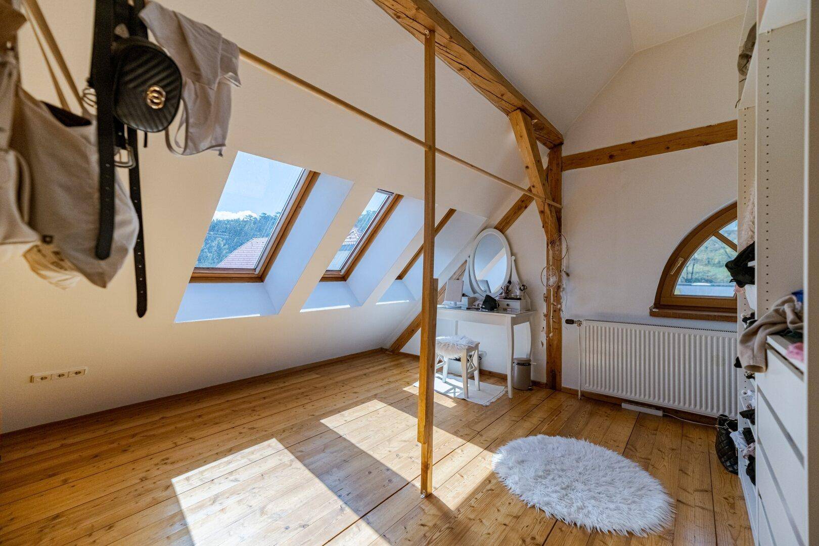 Schlafzimmer im Dachgeschoss mit Holzboden, Dachfenstern und Blick auf die Umgebung.