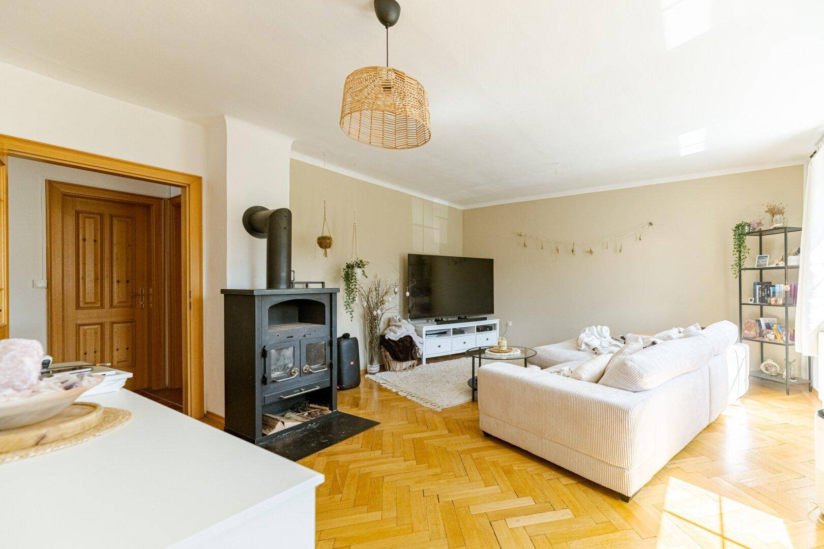Gemütliches Wohnzimmer mit Fischgrätparkett, modernem Holzofen und bequemer Couch.