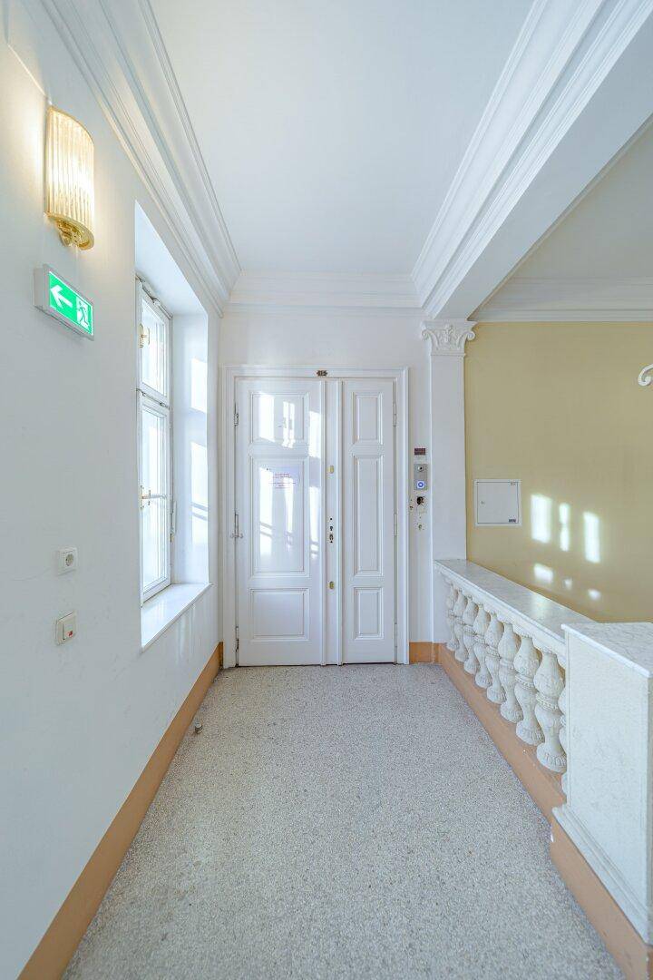 Heller Flur in einem Altbau mit Fenster, weißen Türen und einer klassischen Balustrade.