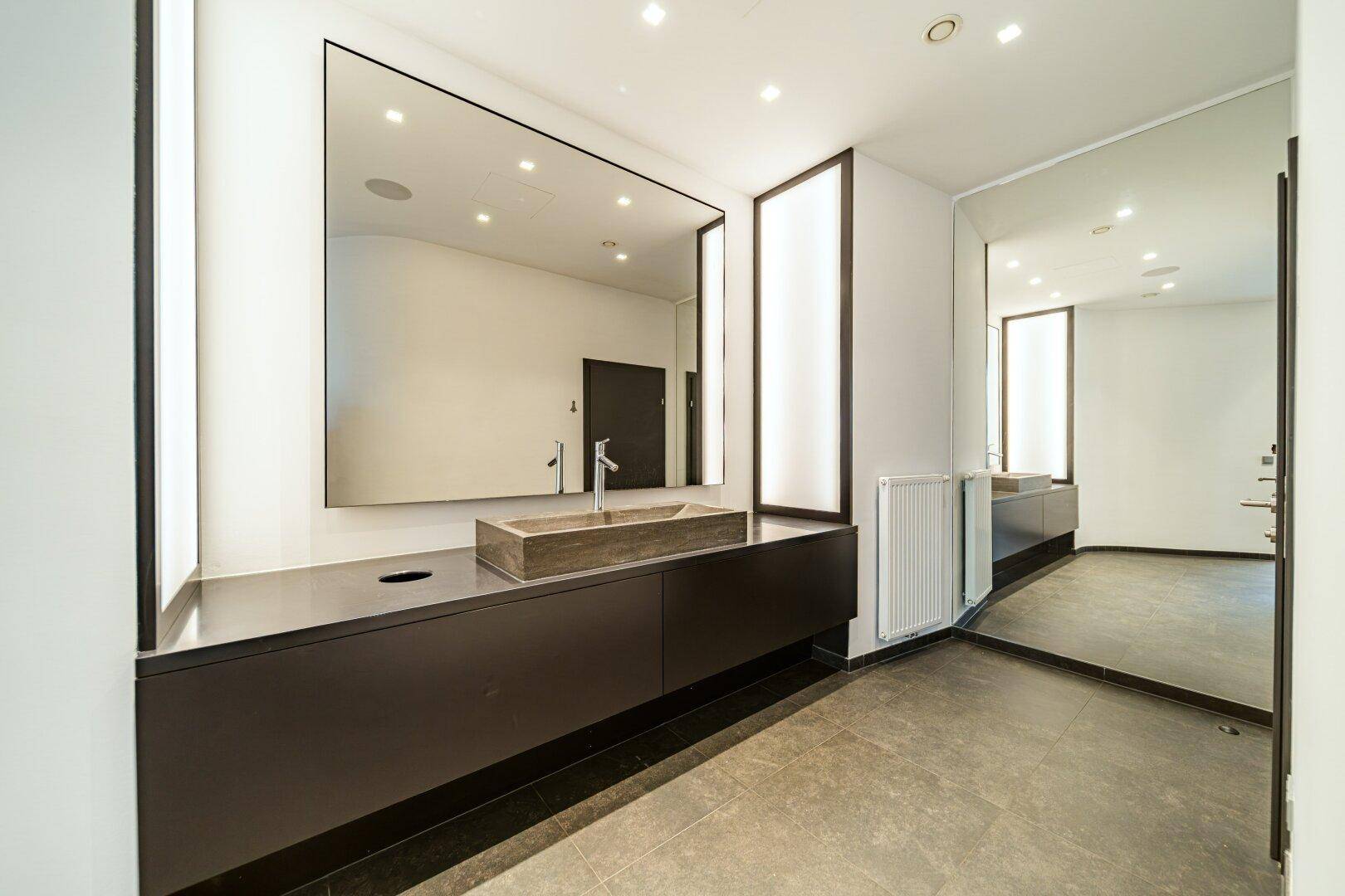 Detailansicht eines modernen Badezimmers mit stilvollem Steinwaschbecken und großem Wandspiegel.