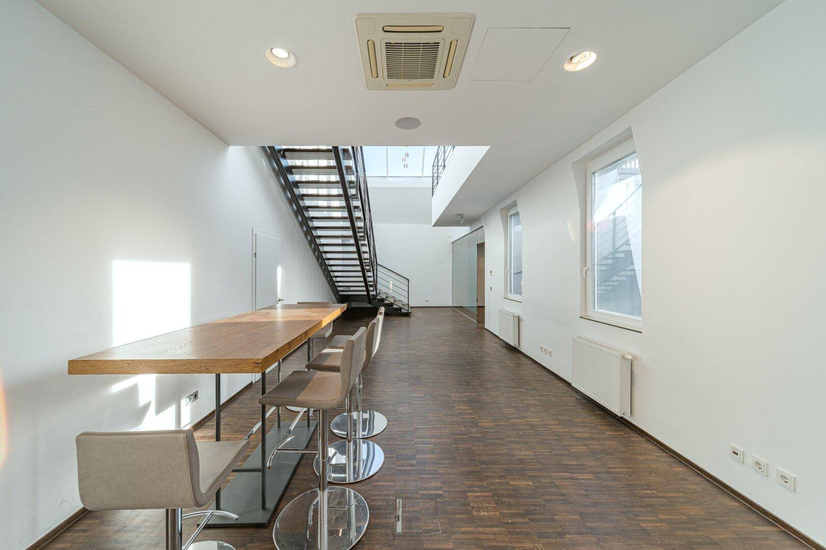 Langer Flur oder Loungebereich mit Bartisch, Hockern und Blick auf eine moderne Treppe.