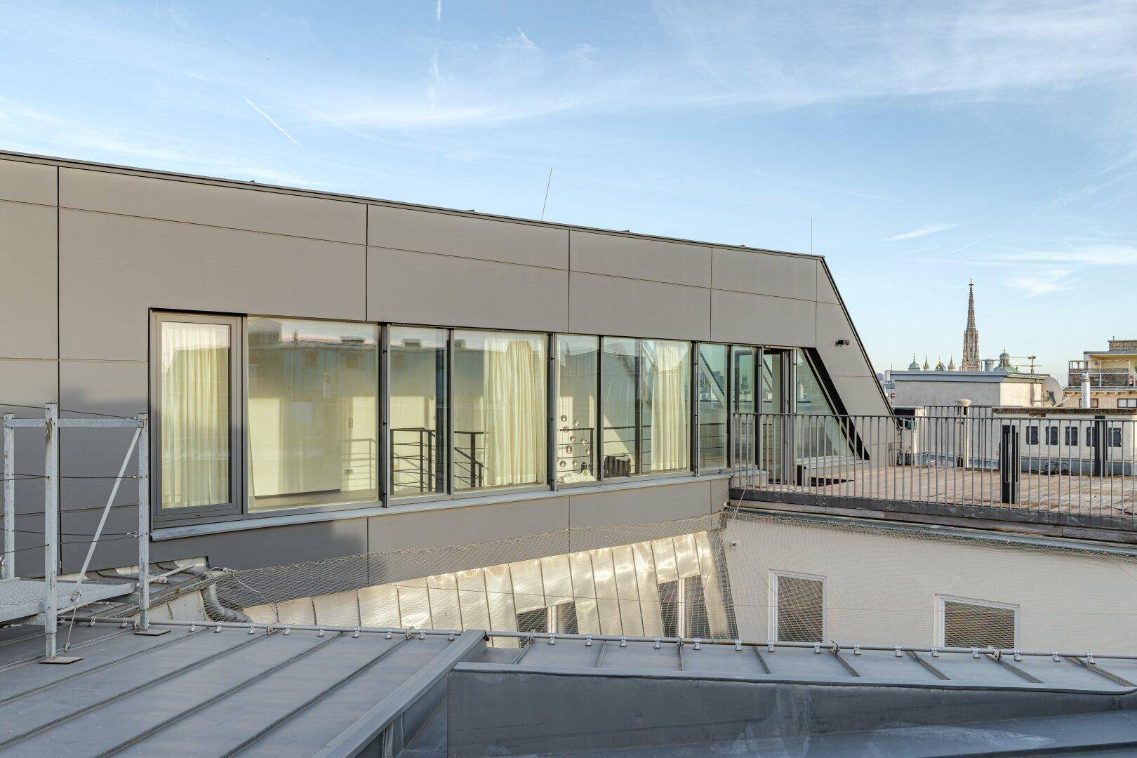 Moderne Gebäudefassade mit großen Fensterfronten und klaren Linien, von einem Dach aus gesehen.