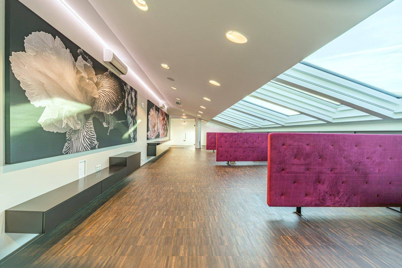 Geräumiger Loungebereich mit schrägen Decken, großen Dachfenstern, Holzboden und farbigen Sitzgelegenheiten.