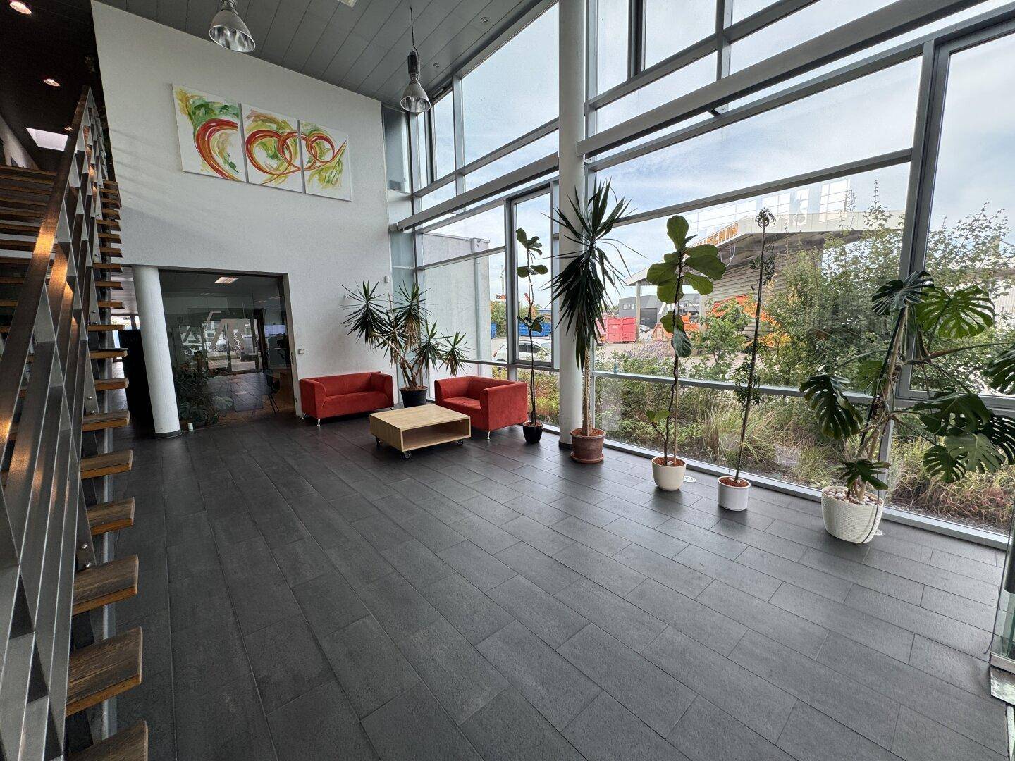 Moderne Eingangshalle mit hohen Decken, großen Glasfronten, einer Treppe und dekorativen Pflanzen.