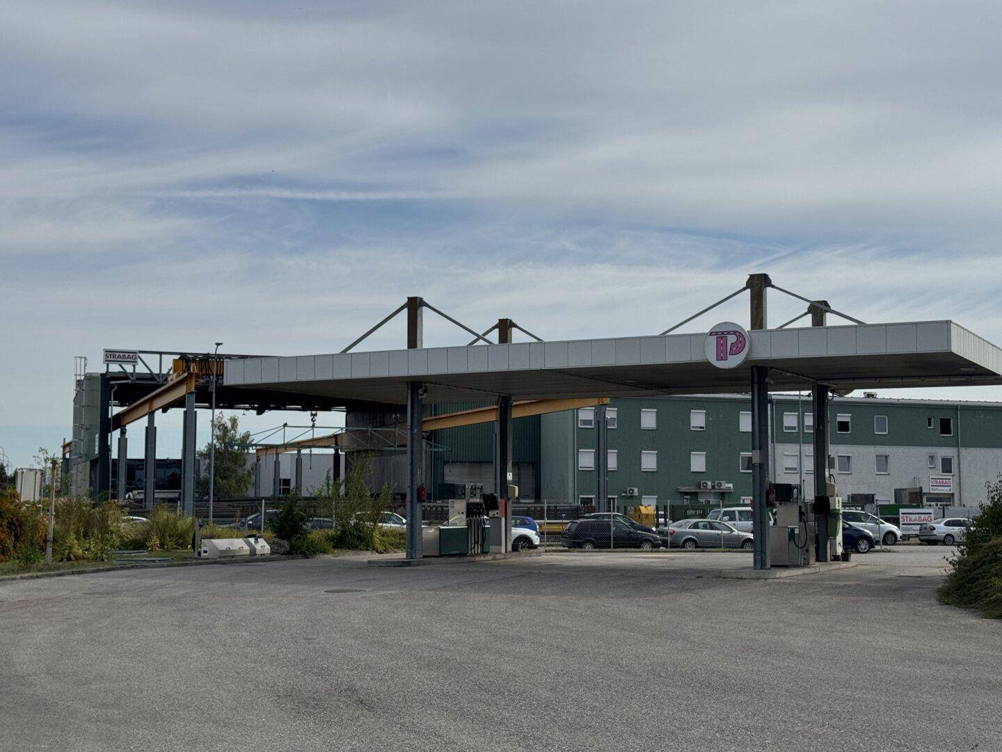 Tankstelle mit Überdachung und Zapfsäulen, umgeben von Parkplätzen und Industriegebäuden.