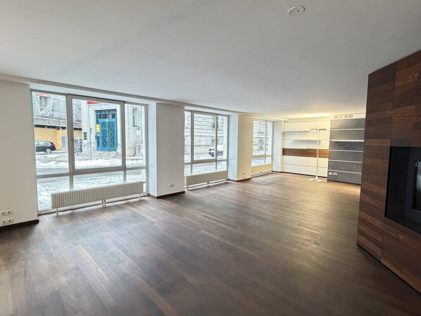 Geräumiger Büroraum mit dunklem Holzboden und großen Fenstern, die viel Licht hereinlassen.