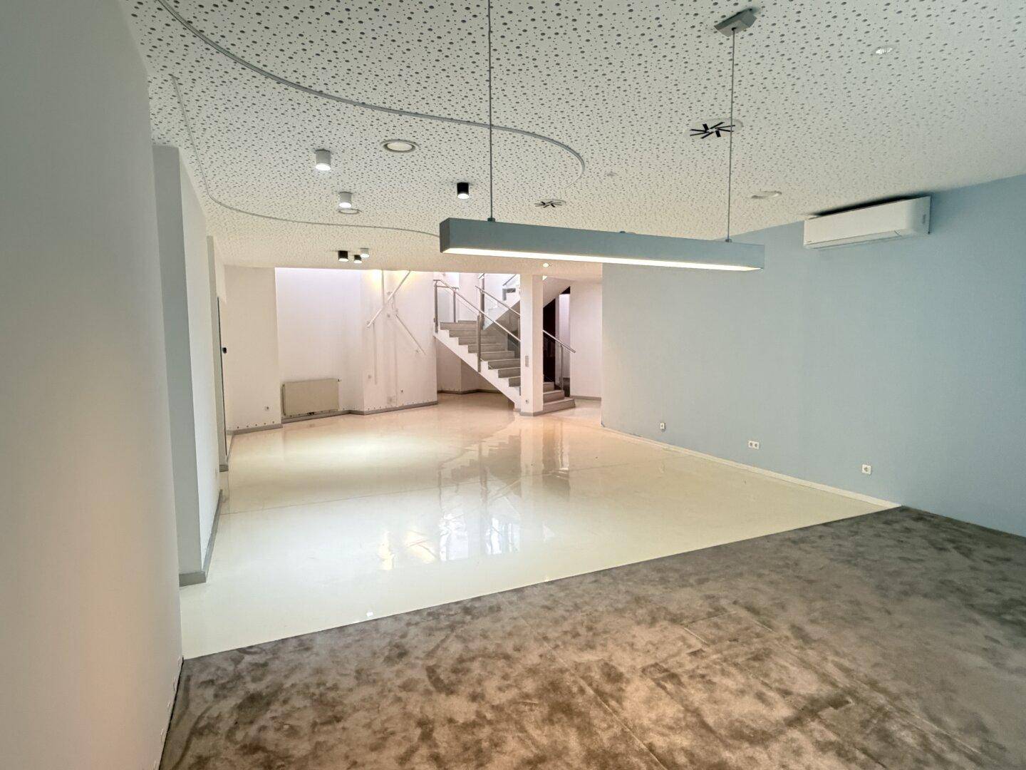 Offener Bürobereich mit unterschiedlichen Bodenbelägen und moderner Beleuchtung, inklusive Treppenaufgang.