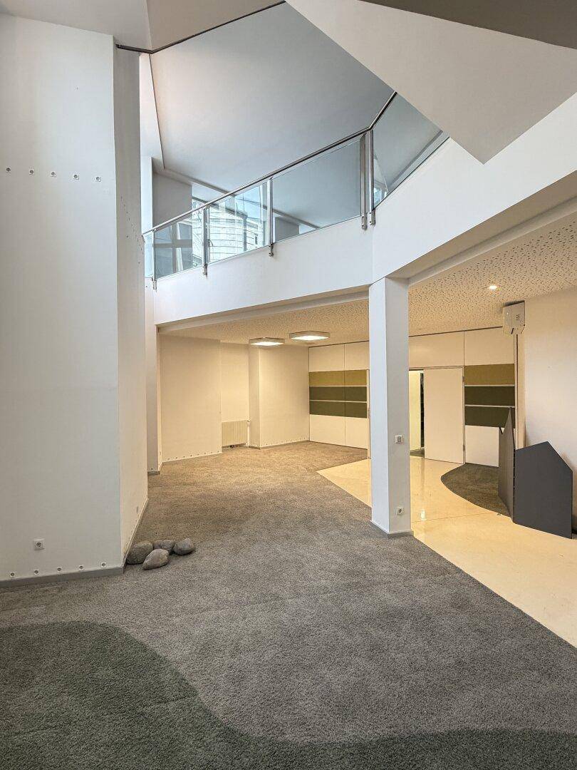 Offener Bürobereich mit Teppichboden und Blick auf eine obere Etage mit Glasgeländer.