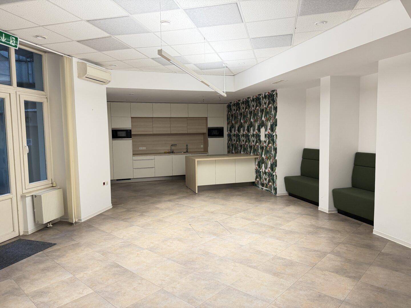 Moderne Büroküche mit Kücheninsel, Einbaugeräten und Sitzgelegenheiten in einem offenen Bereich.