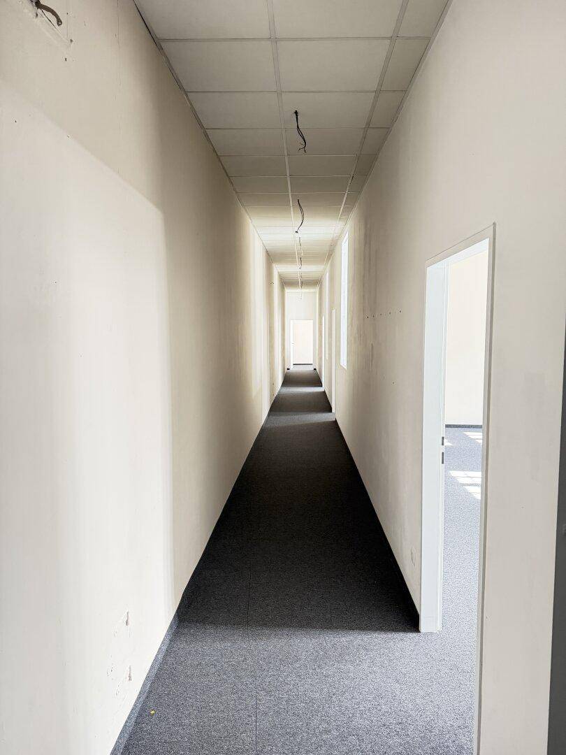 Langer, schmaler Flur mit Teppichboden und abgehängter Decke, der zu weiteren Räumen führt.
