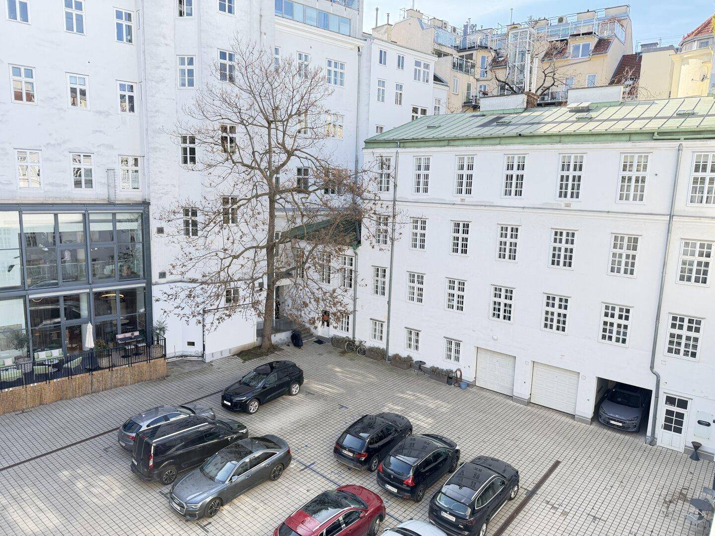 Innenhof mit geparkten Autos und umliegenden weißen Gebäuden, die eine städtische Umgebung zeigen.