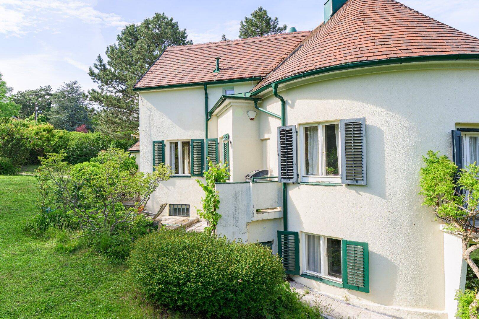 Detailansicht der Hausfassade mit runder Erkerstruktur, grünen Fensterläden und Ziegeldach.