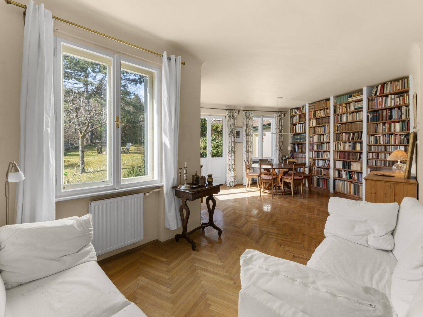 Helles Wohnzimmer mit Parkettboden, Bücherregalen und Blick in den Garten.