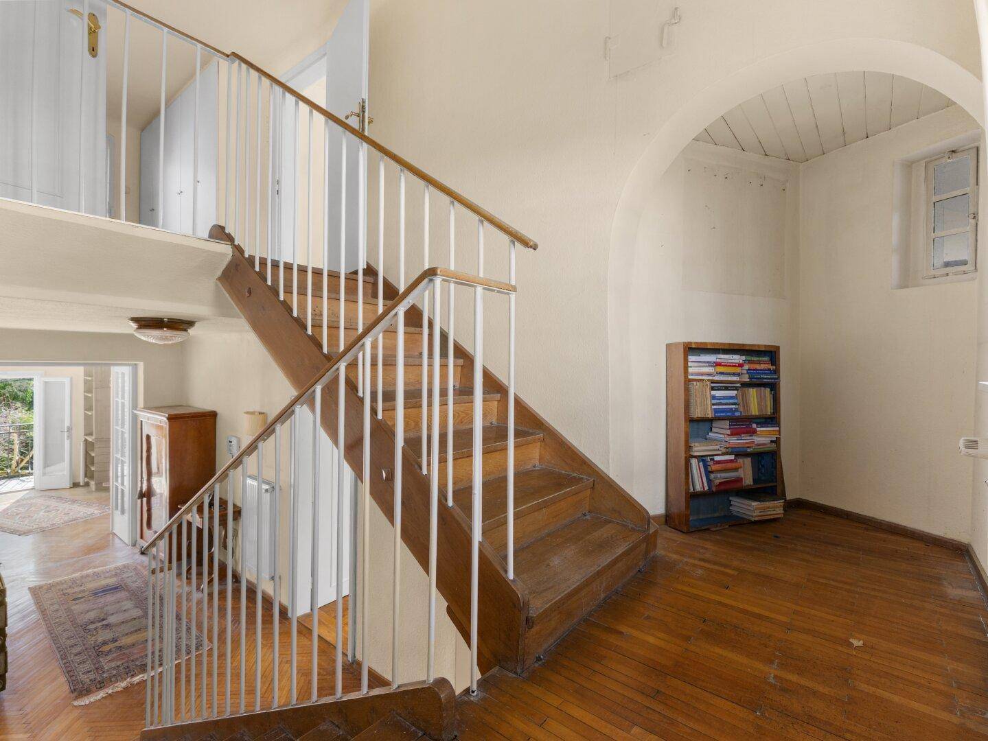 Holztreppe mit weißem Geländer in einem hellen Flurbereich mit gewölbter Decke.