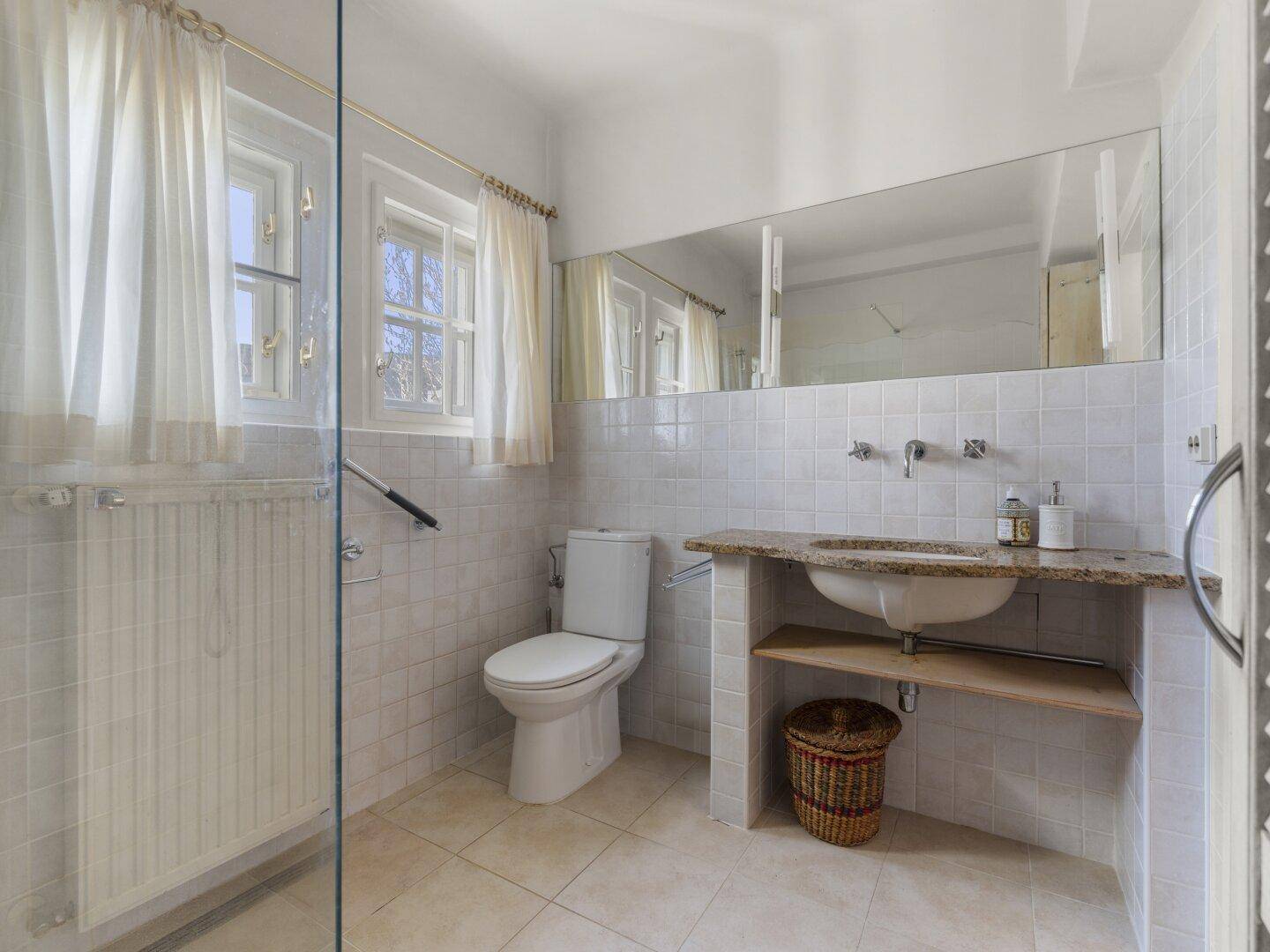 Helles Badezimmer mit Fliesen, Toilette, Waschtisch und Fenster.