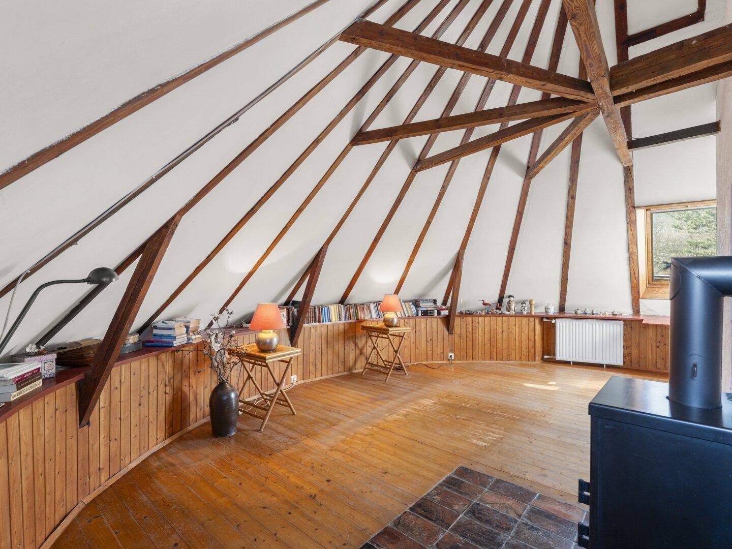 Runder Dachbodenraum mit Holzboden, sichtbaren Dachbalken und Kaminofen.