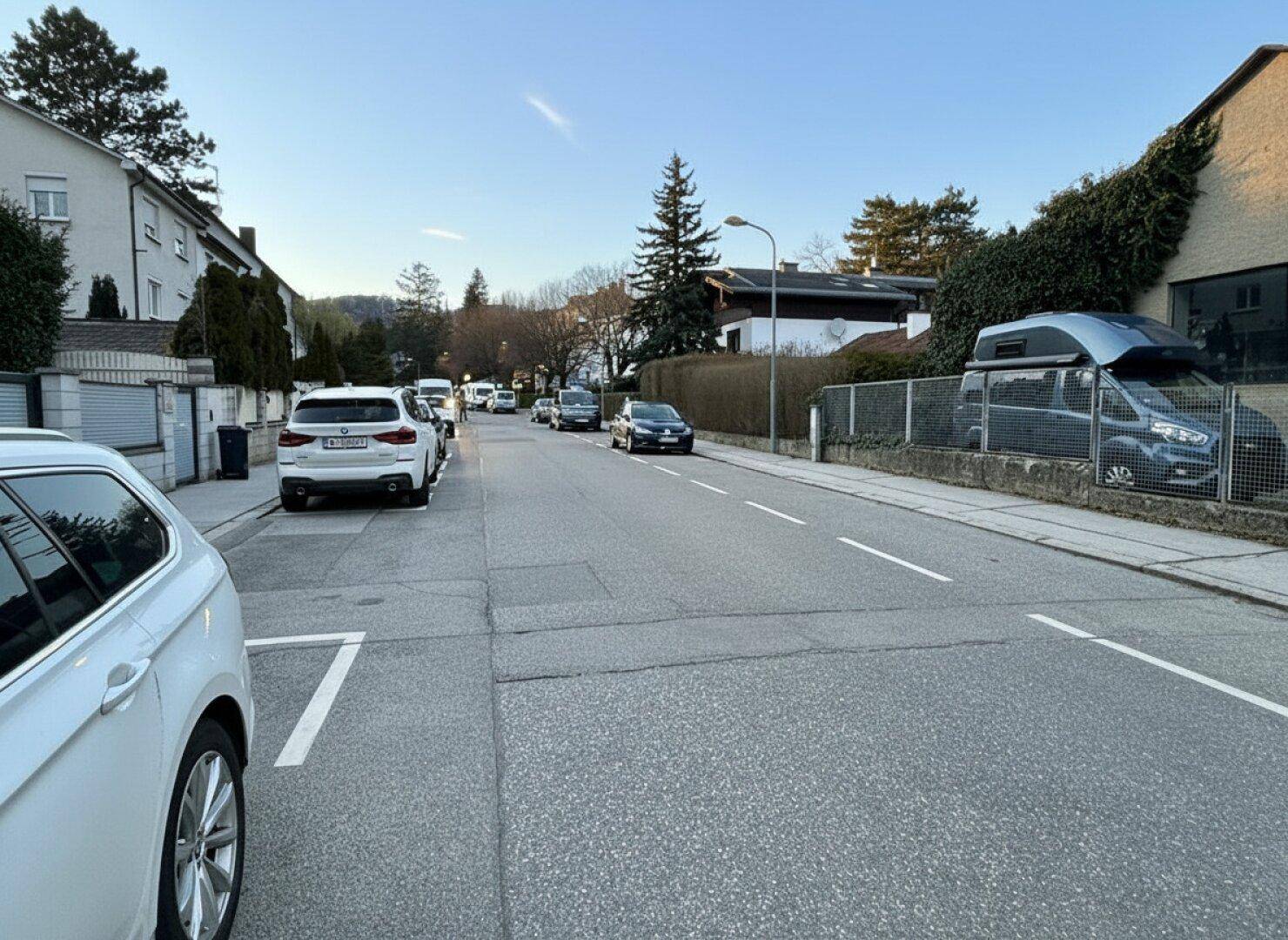 Eine ruhige Wohnstraße mit geparkten Autos und Häusern unter einem klaren blauen Himmel.