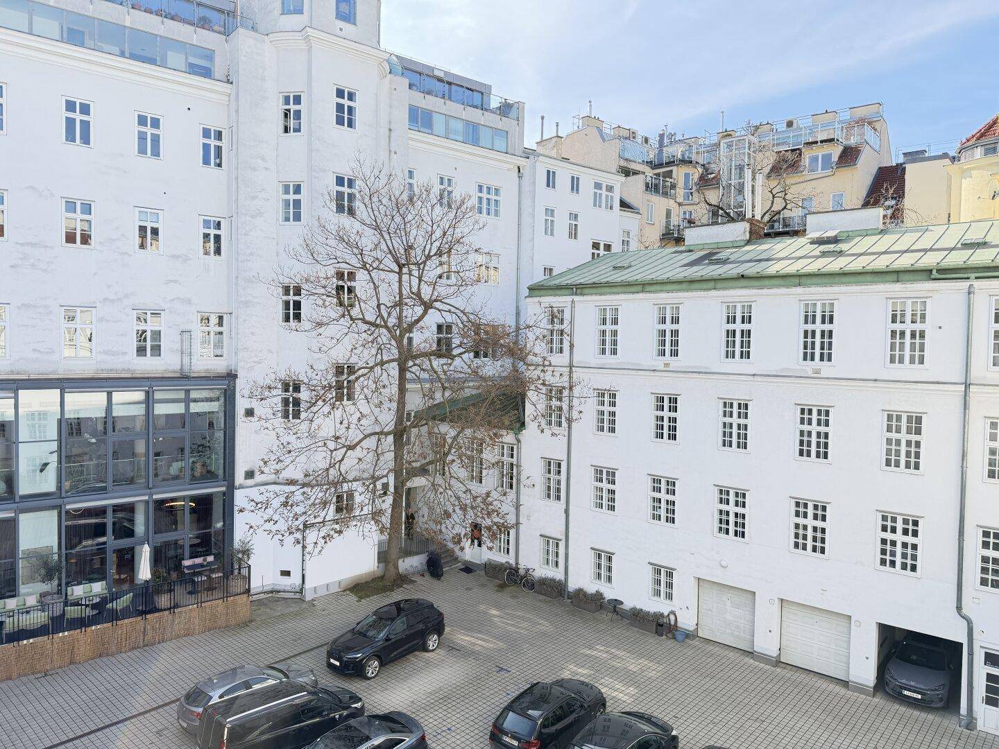 Blick auf einen belebten Innenhof mit parkenden Fahrzeugen, umgeben von hohen, weißen Gebäuden.