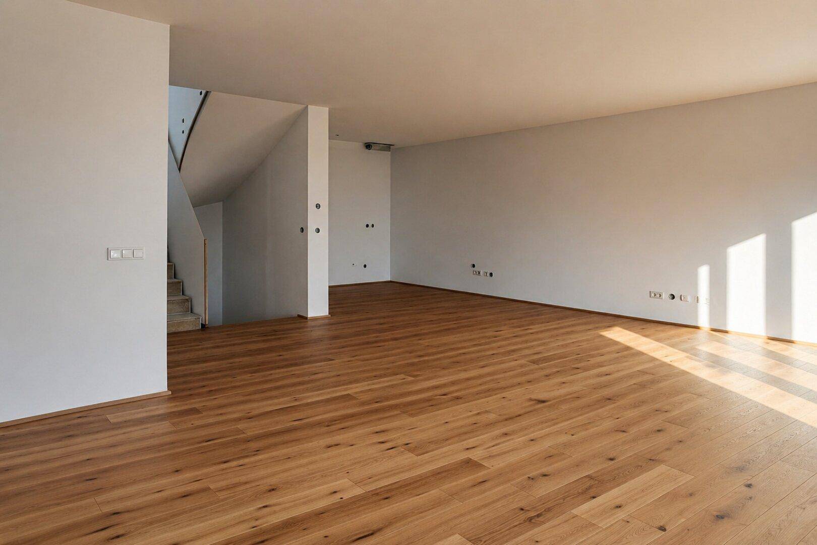Heller, leerer Raum mit Holzboden und Treppe zum Obergeschoss.