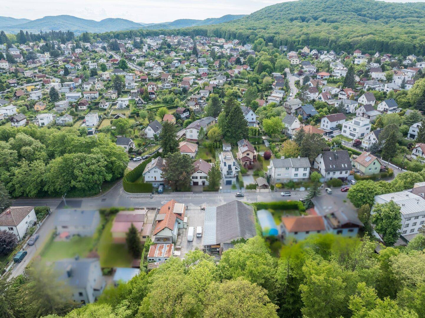 Weitläufige Luftaufnahme eines Wohnviertels mit vielen Einfamilienhäusern und bewaldeten Hügeln im Hintergrund.