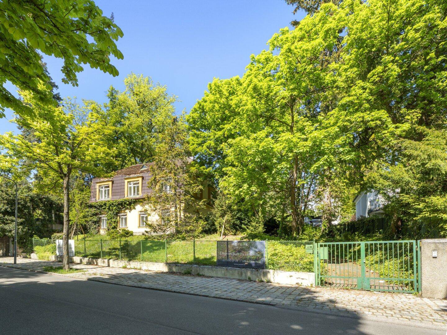 Eingangsbereich des Anwesens von der Straße aus gesehen, umgeben von Bäumen und einem Zaun.