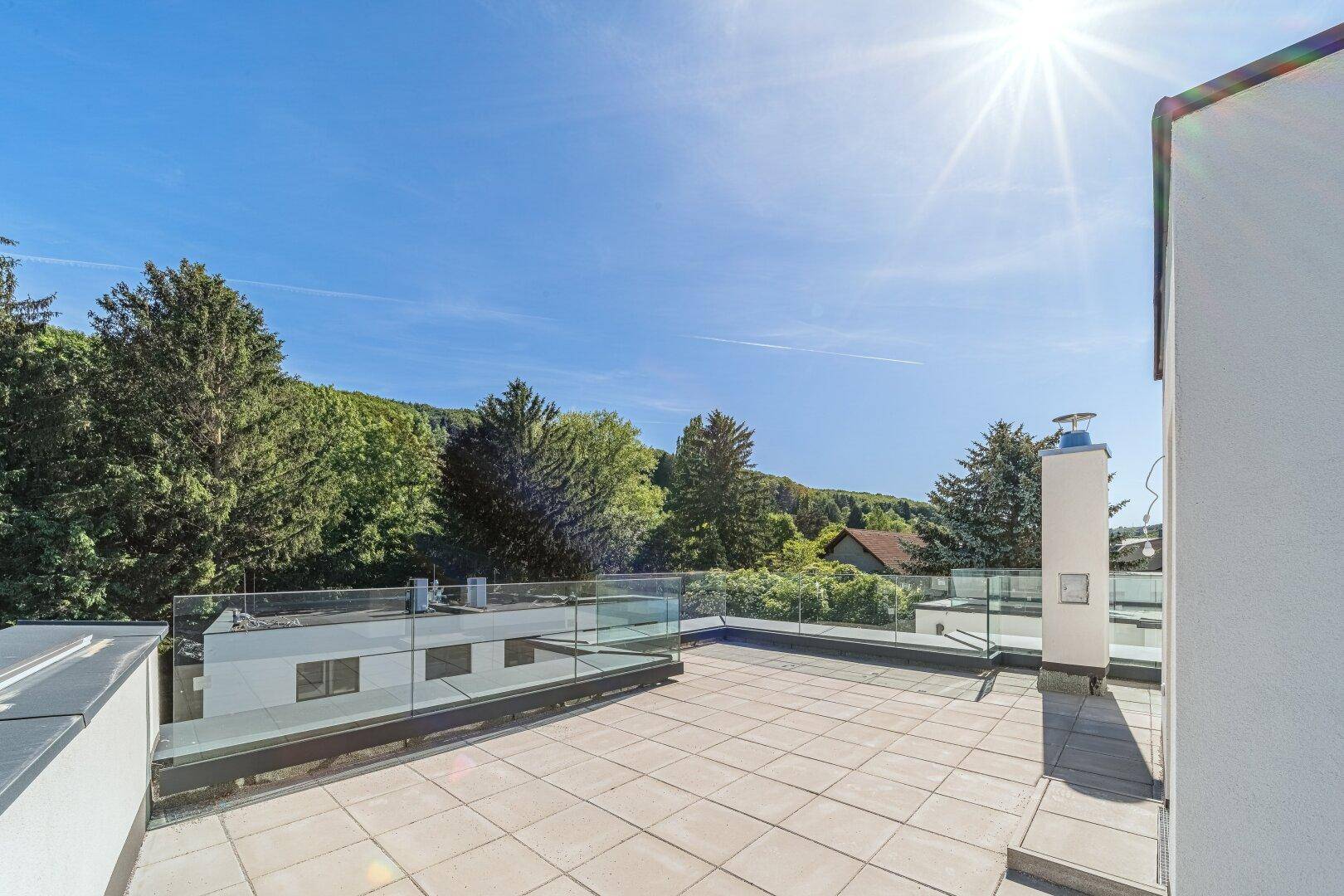 Sonnige Dachterrasse mit weitem Blick ins Grüne und moderner Glasbrüstung.