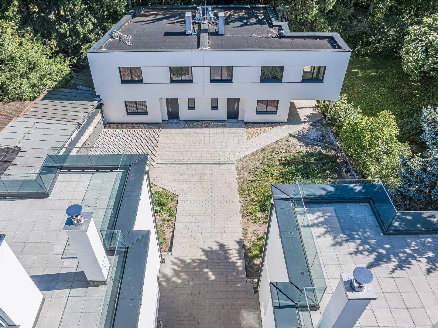 Rückansicht der modernen Gebäude mit gepflasterten Wegen und angrenzendem Grünbereich.