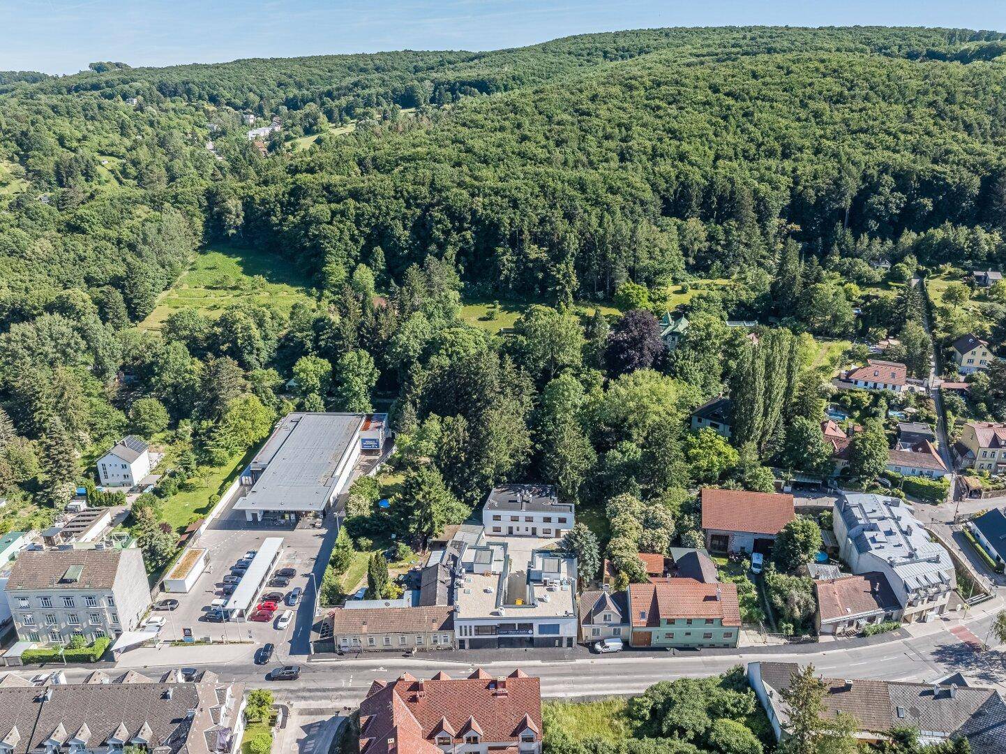 Weitläufige Luftaufnahme der Siedlung mit modernen Gebäuden und umgebendem Waldgebiet.