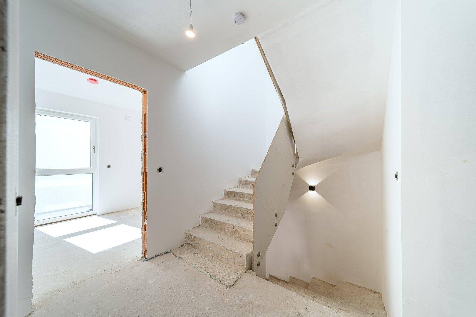 Heller Treppenaufgang in einem Neubau mit schlichtem Design und indirekter Beleuchtung.