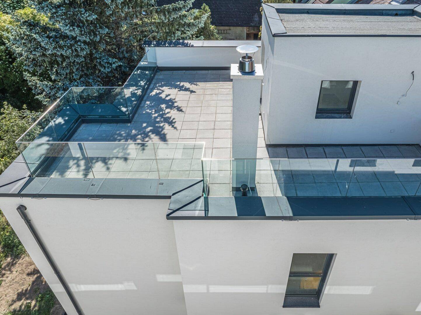 Moderne Dachterrasse mit Glasgeländer und hellen Fliesen, ideal für Entspannung im Freien.