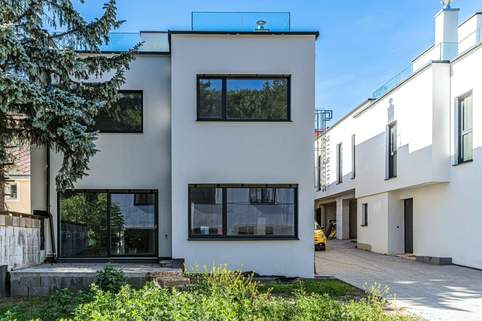 Außenansicht eines modernen Neubaus mit großen Fenstern und klaren Linien in sonniger Umgebung.