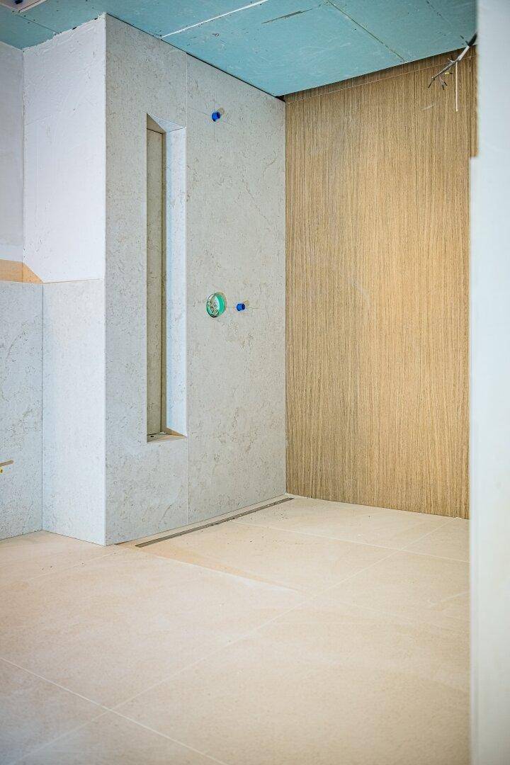 Unfertiges Badezimmer mit gefliestem Boden und vorbereiteter Duschzone, bereit für die Endmontage.