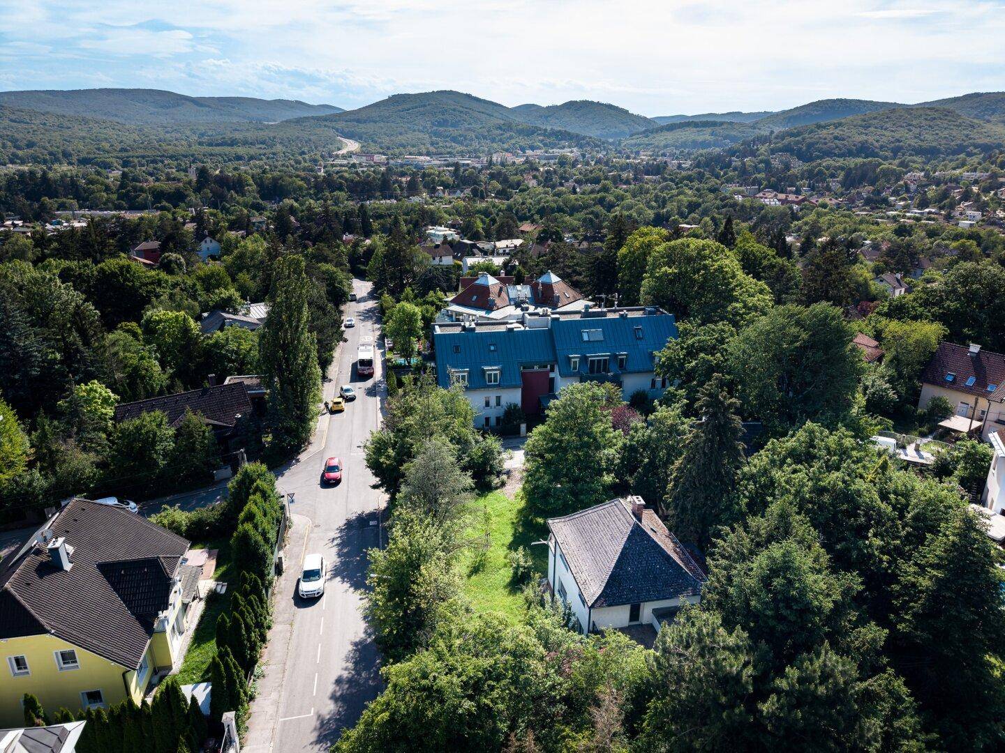 Weitläufige Luftaufnahme der grünen Umgebung mit Häusern und Bergen im Hintergrund.