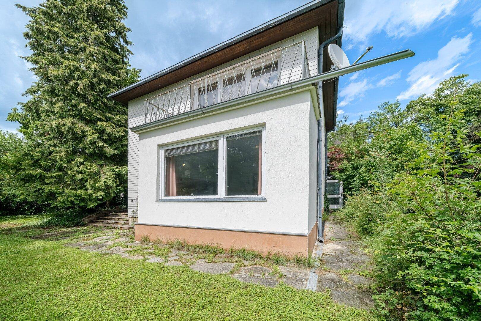 Seitenansicht des Hauses mit Balkon im Obergeschoss und Gartenbereich im Vordergrund.