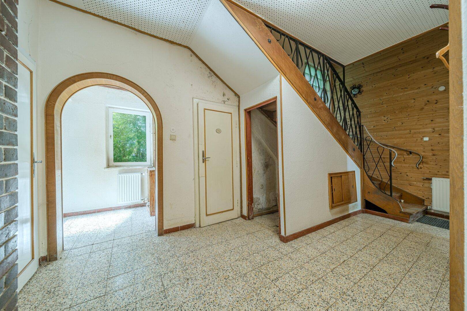 Geräumiger Flur mit Fliesenboden, Holztäfelung und einem Rundbogen zu einem weiteren Raum.