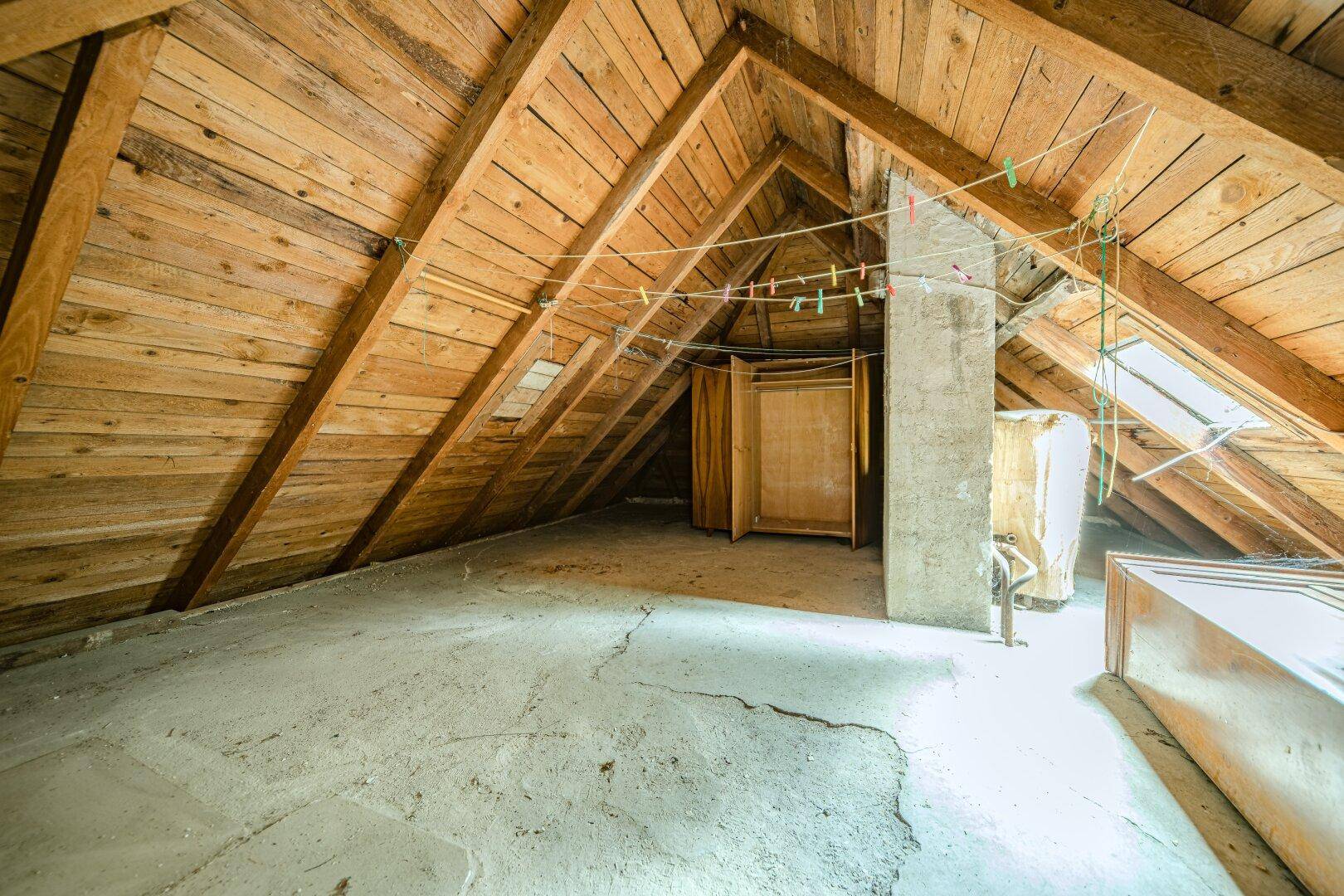 Geräumiger Dachboden mit sichtbaren Holzbalken und Dachfenstern, ideal für Ausbau.