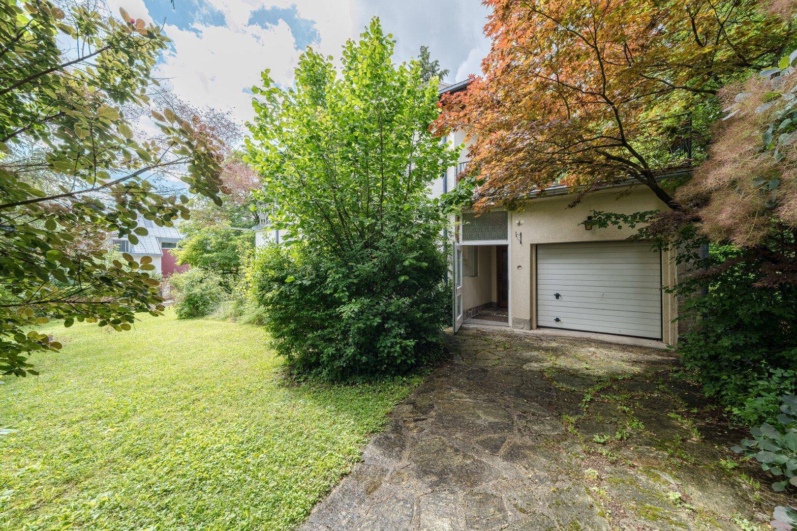 Einfahrt zur Garage mit angrenzendem Gartenbereich und altem Baumbestand.