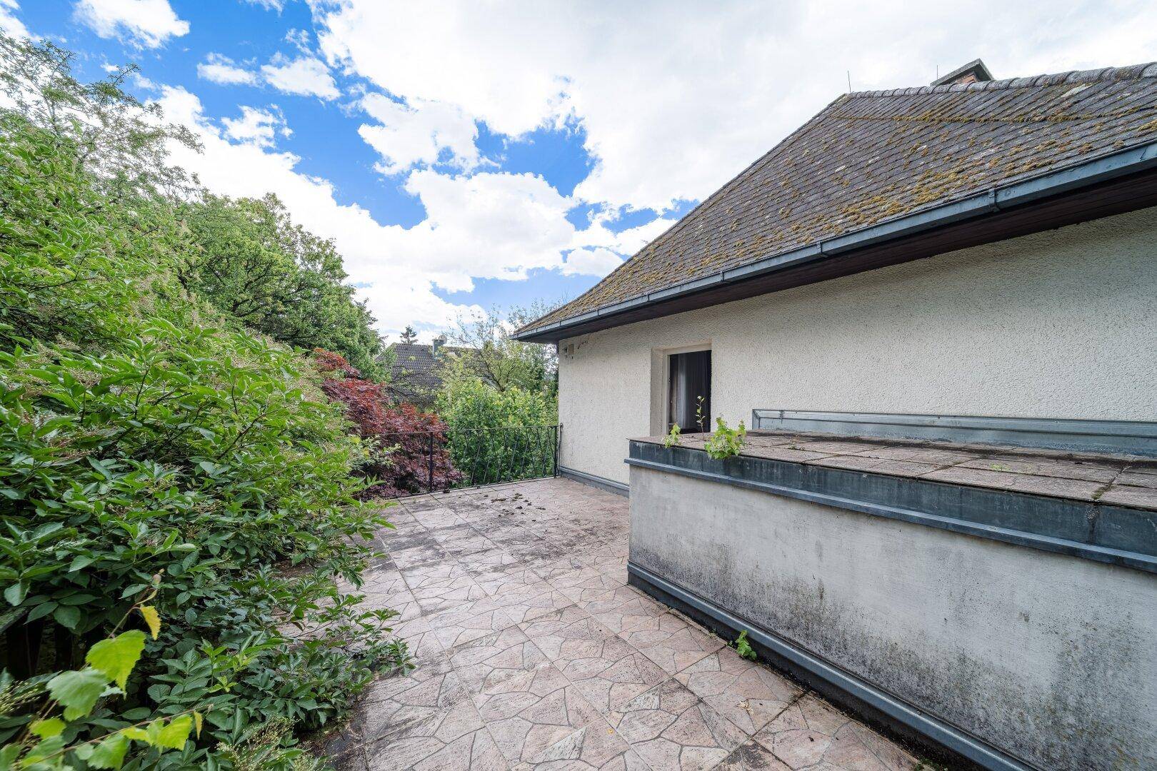 Gepflasterte Terrasse am Haus, umgeben von Grün, mit Potenzial für eine gemütliche Sitzecke.