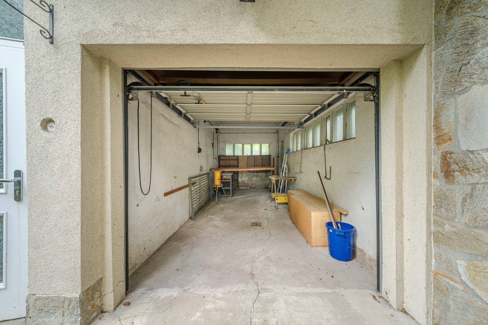Geräumige Garage mit Werkbank und Fenstern, nutzbar als Werkstatt oder Abstellraum.