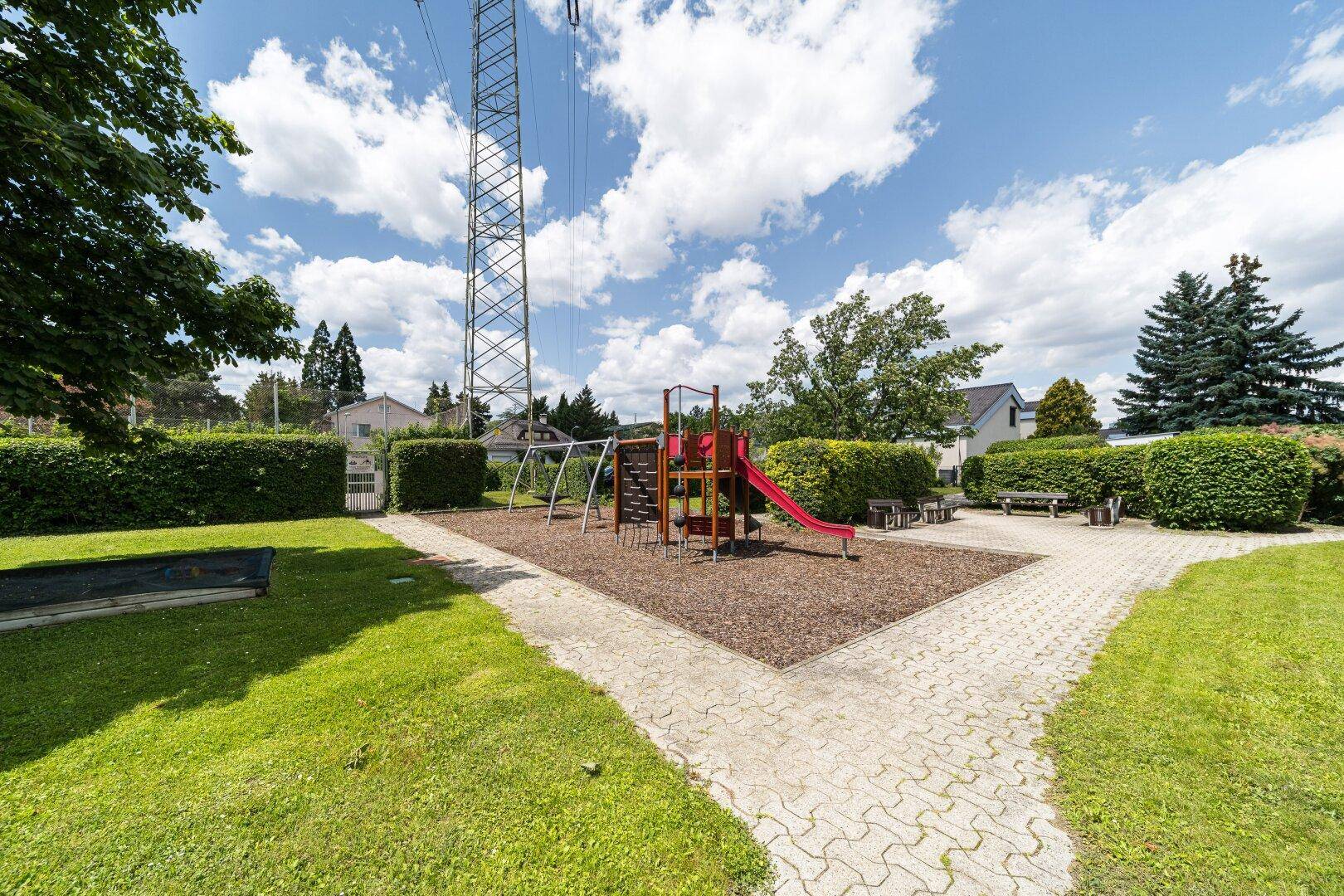 Öffentlicher Spielplatz mit Rutsche und Schaukeln, umgeben von Grünflächen und Hecken.